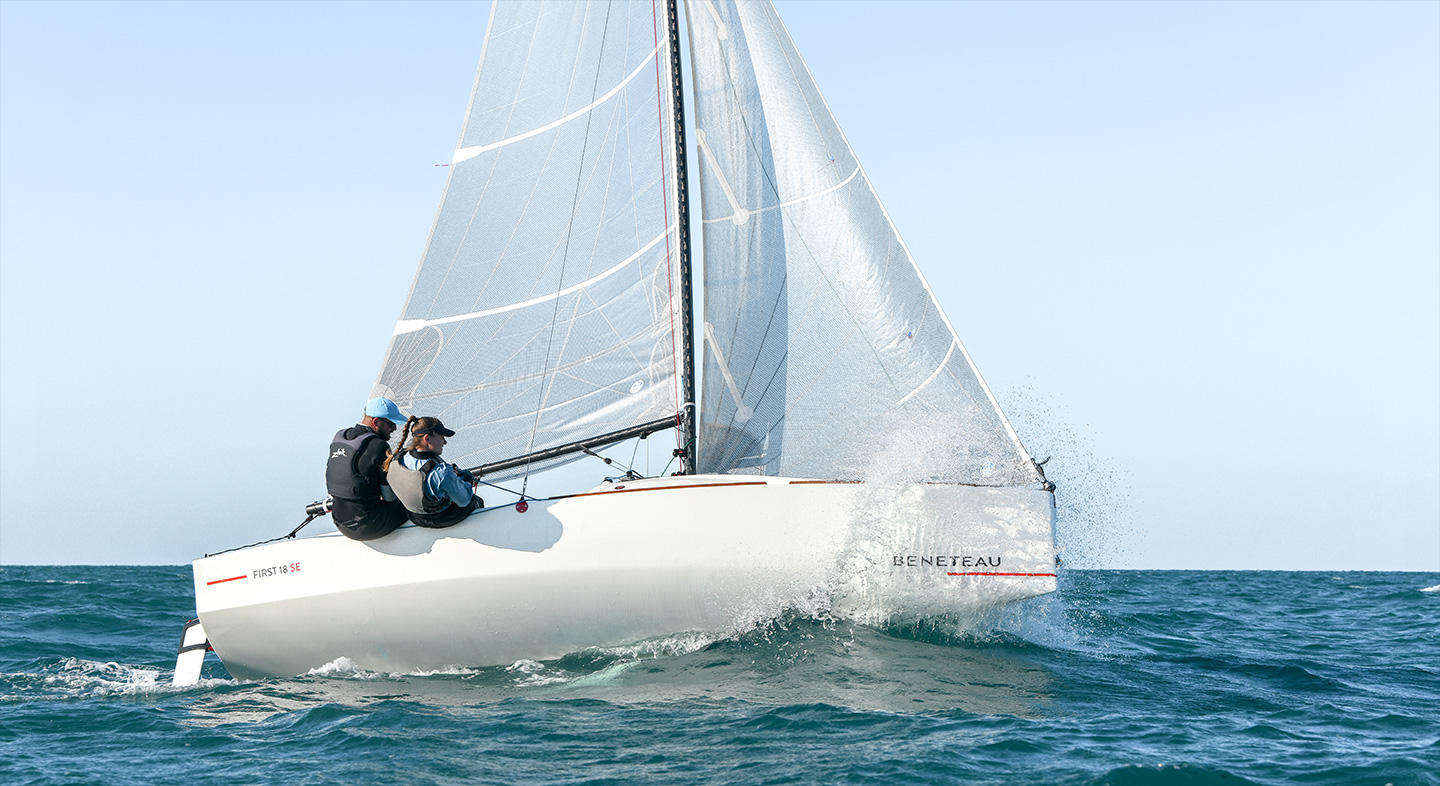 Bateau Bénéteau first 18 SE qui navigue vu de dos. Il y a 2 personnes à son bord.