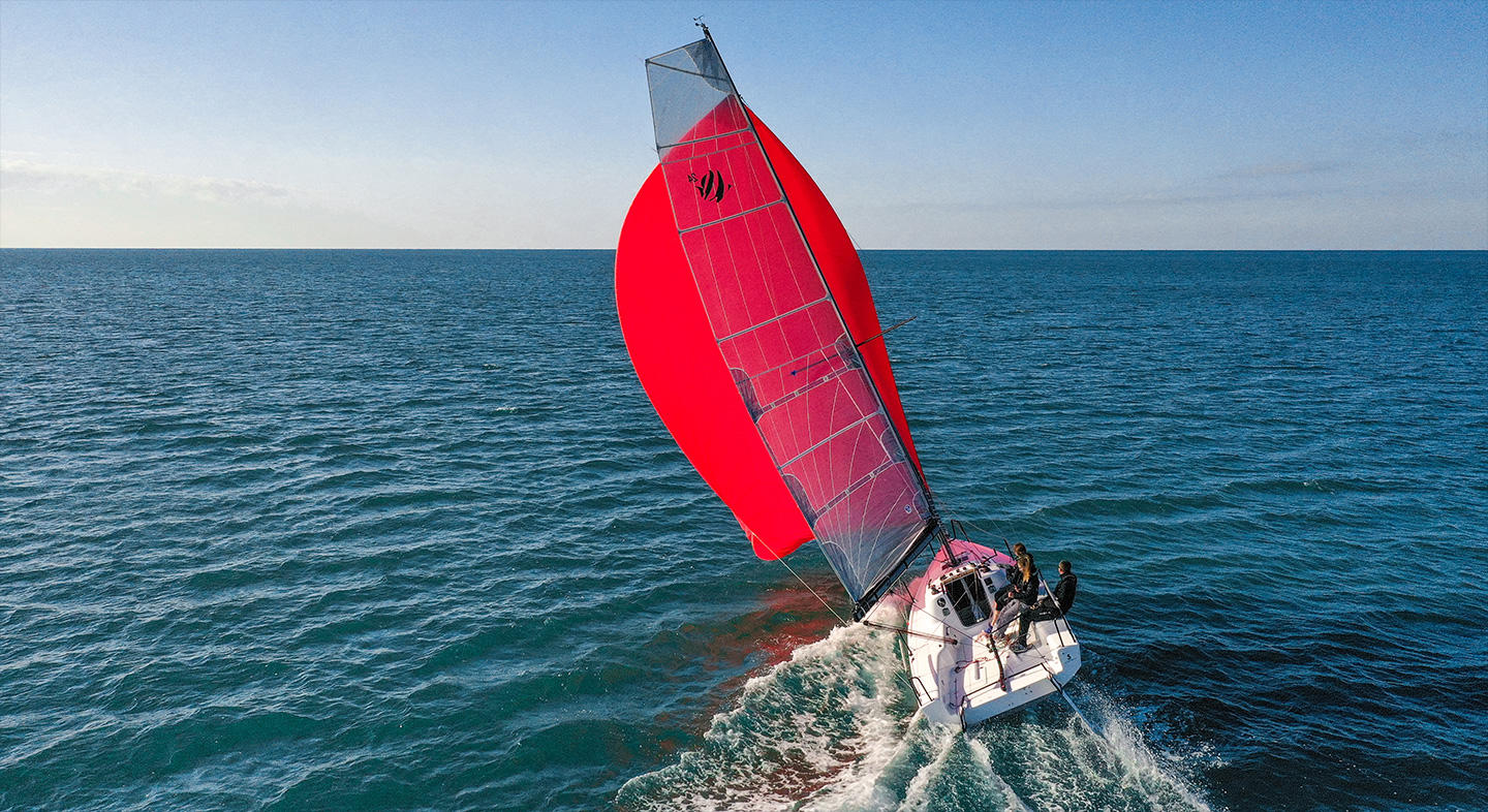 Photo du First 24 SE naviguant avec 4 personnes à son bord. Ses voiles sont déployées et elles ont une prise au vent. C'est le bateau idéal pour les régate ou les sortie en famille.