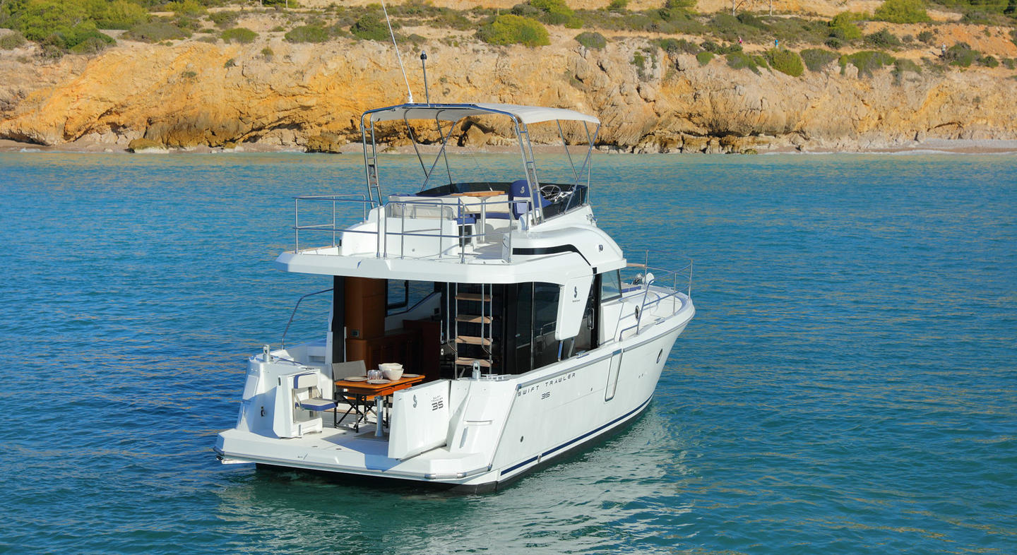 Photo du Swift Trawler 35 naviguant sur l'eau. Ce bateau possède une carène semi planante, un espace habitable, et un bimini ou soft top. Il y a une échelle relient la partie supérieur du bateau à la partie inférieure.